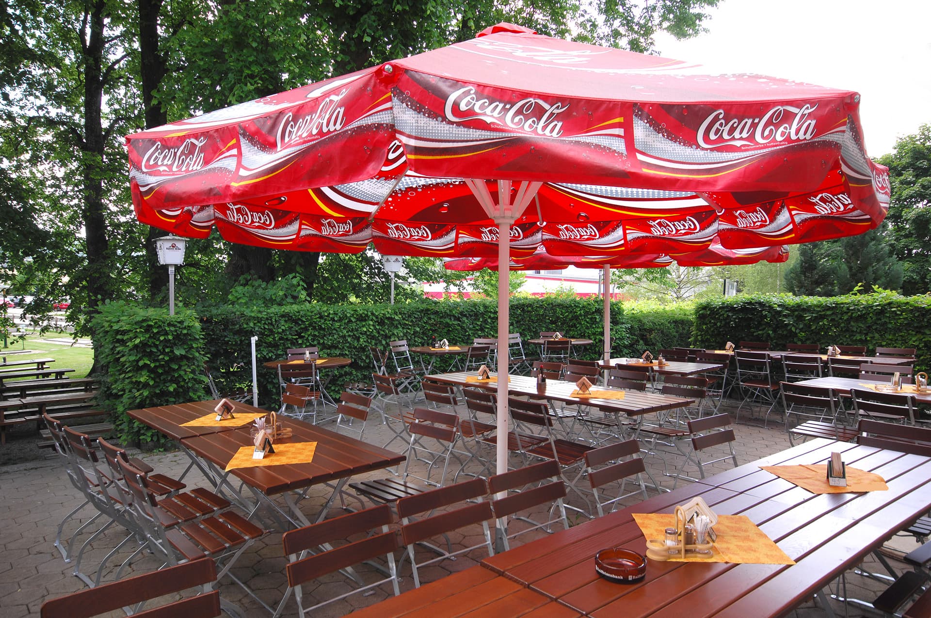 Biergarten mit Tischen und einem roten Sonnenschirm