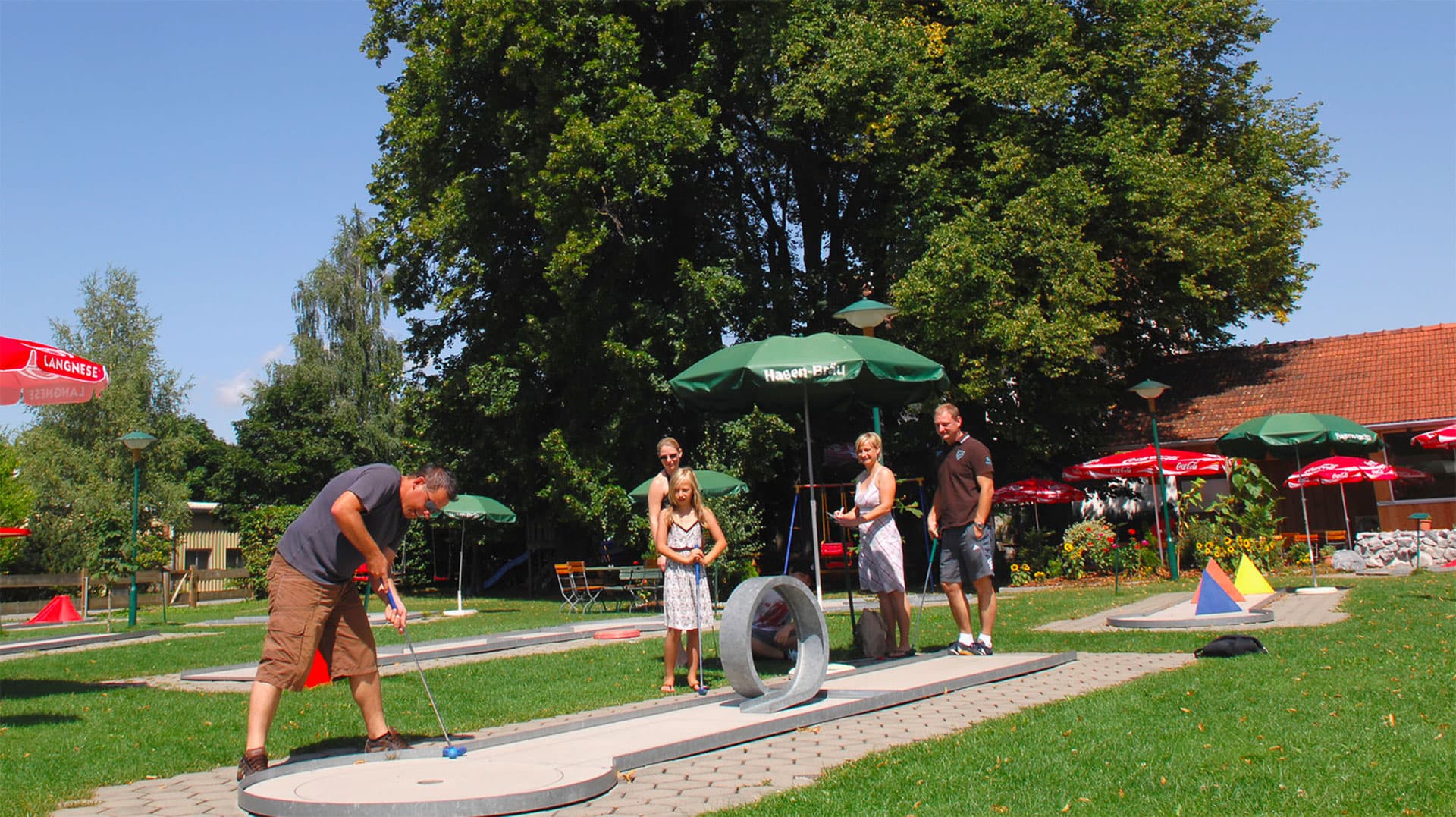 Spieler auf der Minigolfbahn zwischen Sonnenschirmen