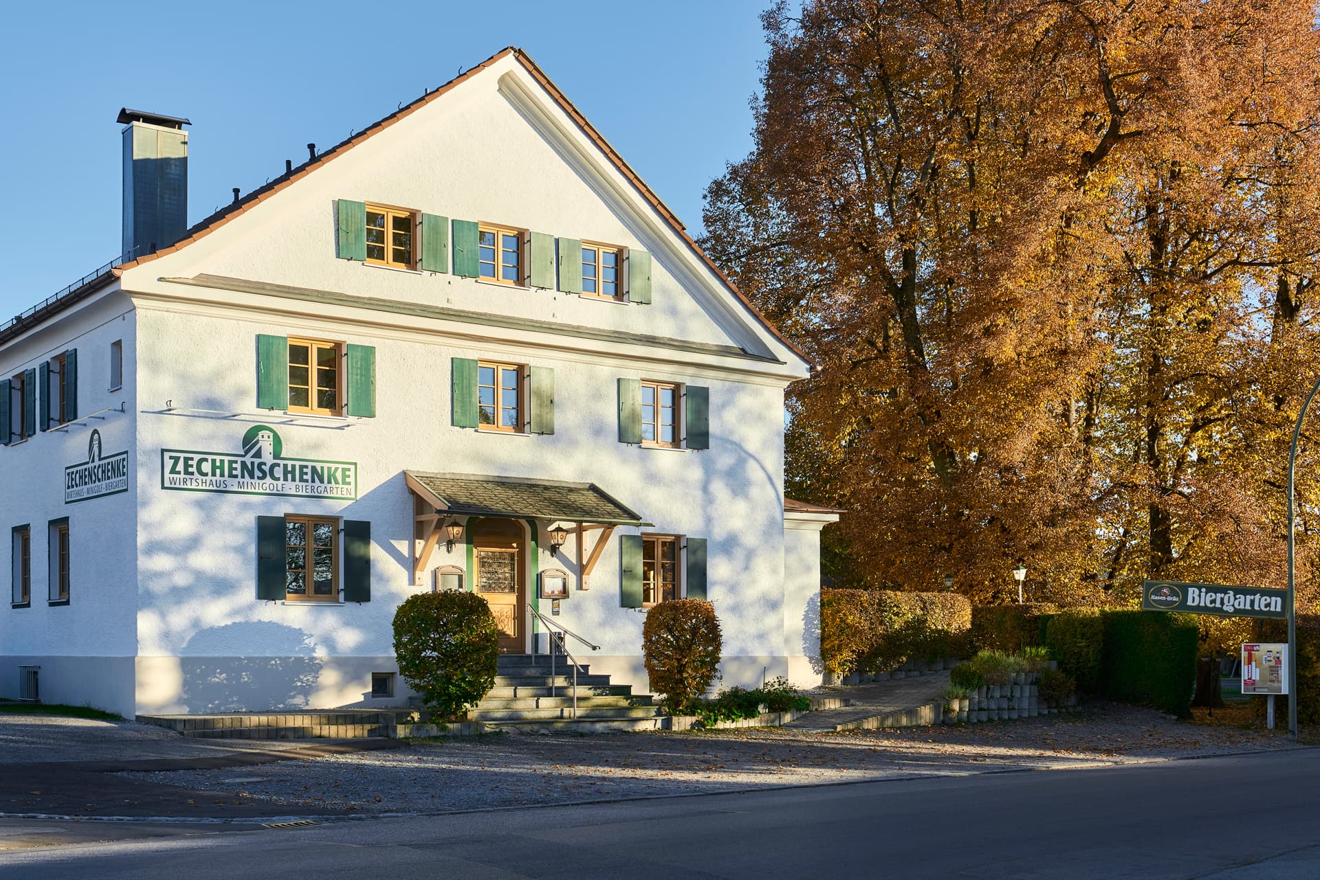 Der Gasthof Zechenschenke in Peiting im Herbst, davor Bäume in Herbstfarben
